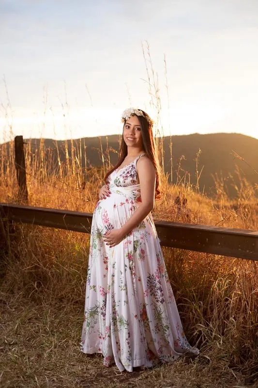 Gestante de vestido florido no campo, ao pôr do sol